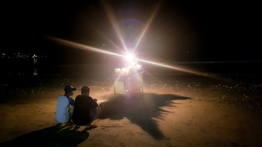 Jeunes hommes devant une carriole de snacks sur la plage de Jimbaran, Bali