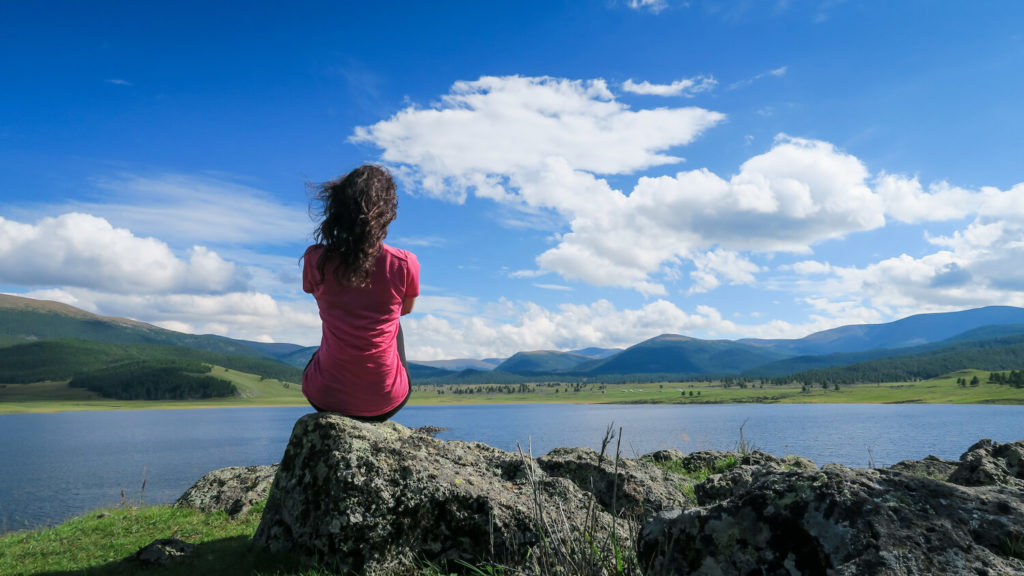 Femme assise de dos devant un lac en Mongolie