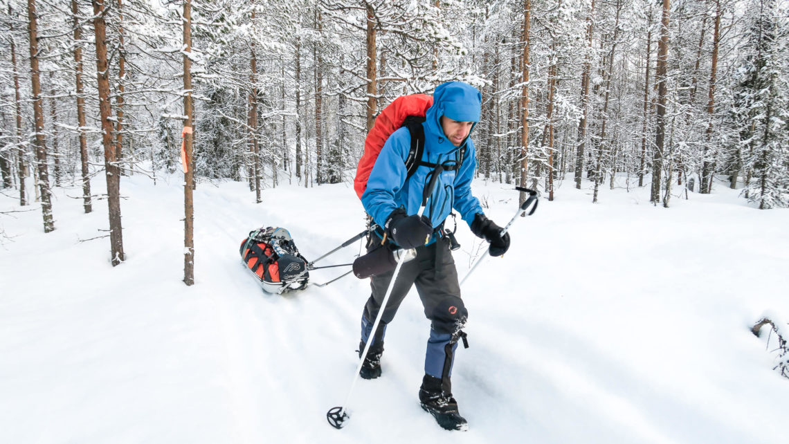 Homme qui marche sur un sentier enneigé en forêt en traînant une pulka