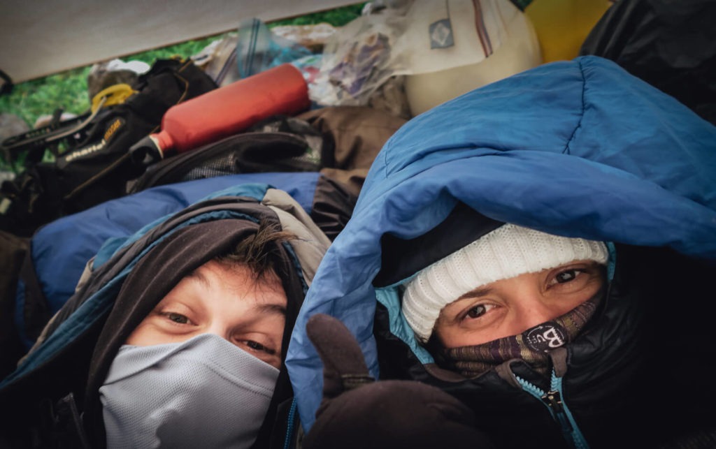Deux personnes dans leurs duvets sous la tente, en montagne, le cache-col remonté sur le nez