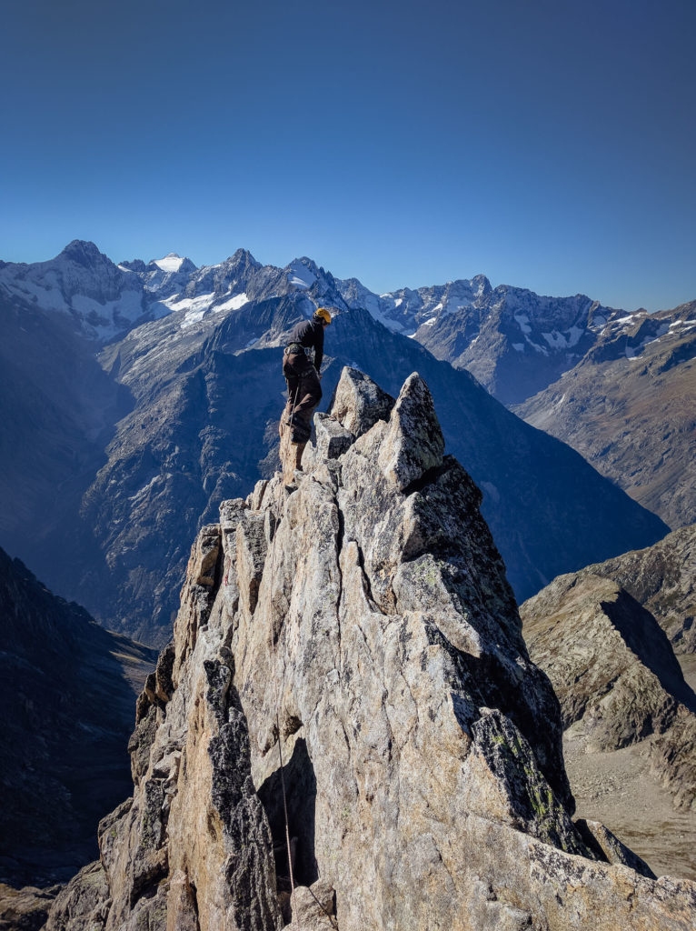 Une personne arrive au sommet de l'Aiguille Dibona sur fond de ciel bleu