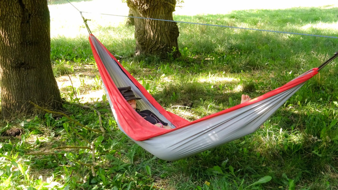Je fais la sieste avec un chapeau sur le nez, dans un hamac tendu entre deux gros arbre sur un pré d'herbe verte