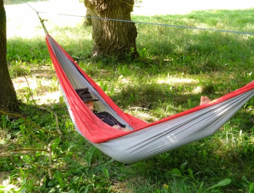 Je fais la sieste avec un chapeau sur le nez, dans un hamac tendu entre deux gros arbre sur un pré d'herbe verte