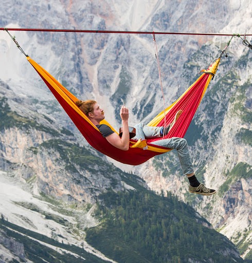 Homme installé dans un hamac suspendu au-dessus du vide, dans les montagnes