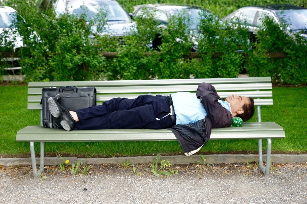 Un homme fait une sieste dans un parc, allongé sur un banc