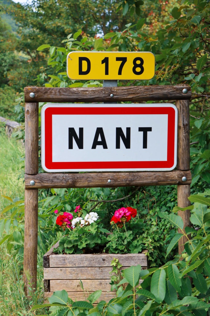 Panneau de signalisation du village de Nant avec géraniums où il est bon de faire un stop lors d'un weekend en Aveyron