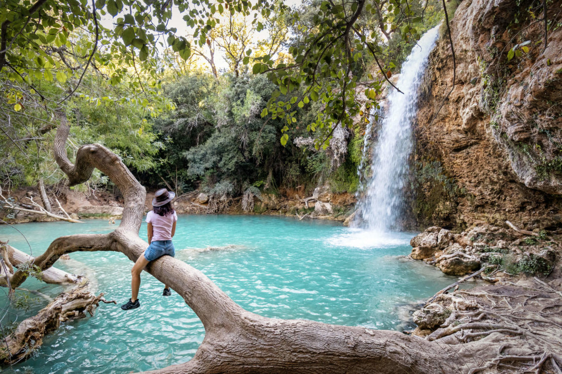 Femme avec chapeau assise sur un tronc d'arbre près de la petite cascade de Sillans