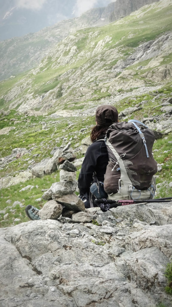 Je suis assise sur un rocher en montagne près d'un cairn, avec mon sac à dos