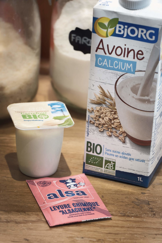 Lait d'avoine, yaourt de soja et levure chimique disposés pour une recette de pancakes vegan