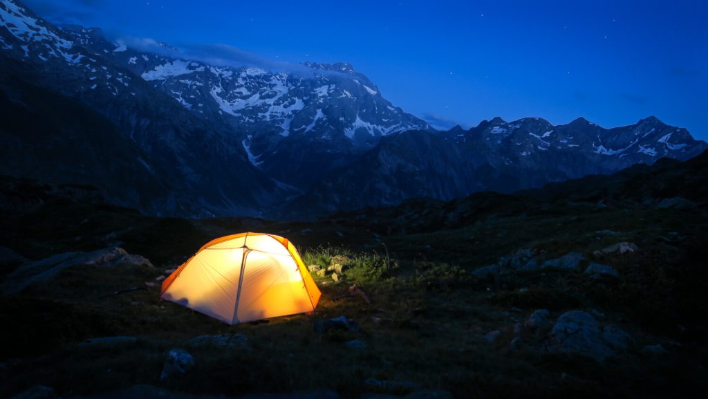 Tente éclairée de l'intérieur sur emplacement de bivouac à la tombée de la nuit, en montagne
