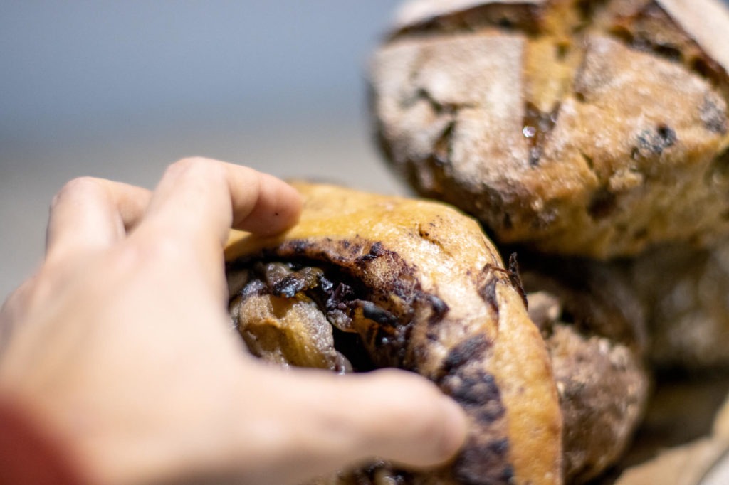 Main saisissant un pain roulé aux olives et oignons confits